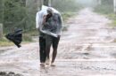Man covered in a plastic sheet walking through heavy rain and strong wind on a muddy road