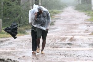 Man covered in a plastic sheet walking through heavy rain and strong wind on a muddy road