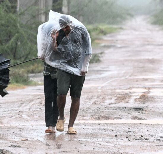 Man covered in a plastic sheet walking through heavy rain and strong wind on a muddy road