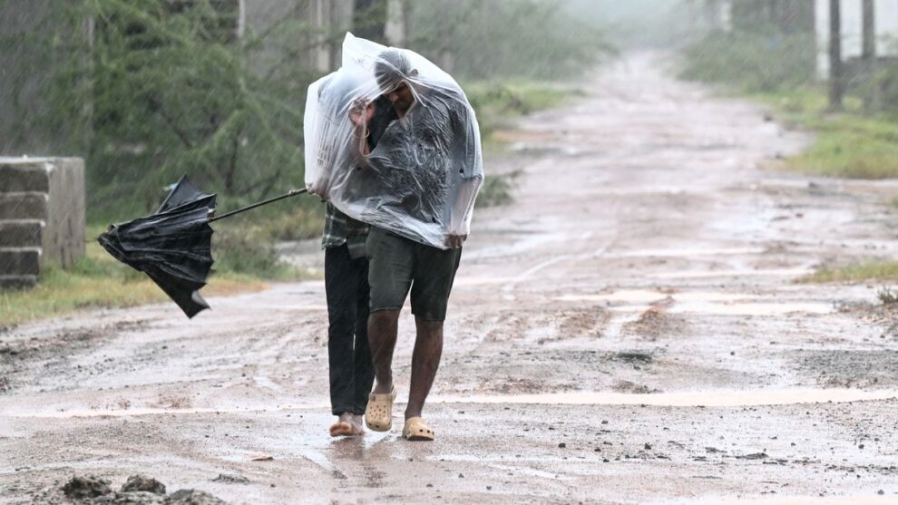 Man covered in a plastic sheet walking through heavy rain and strong wind on a muddy road