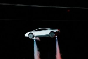 White new Tesla Roadster airborne at night with cold-gas thrusters firing beneath the wheels